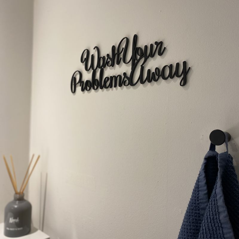 Vægdekoration med citatet "Wash Your Problems Away" i sort mat akryl, 31 cm lang og 10 cm høj.